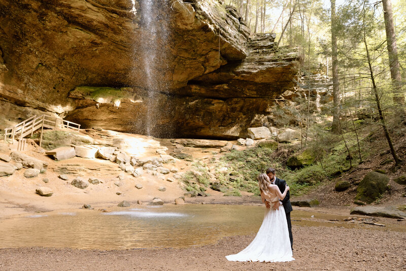 Elopement couple embracing in front of the Ash Cave waterfall.