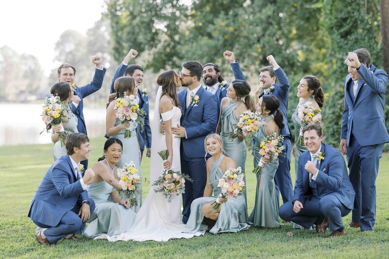 bride and groom kissing as the bridesmaids and groomsmen celebrate