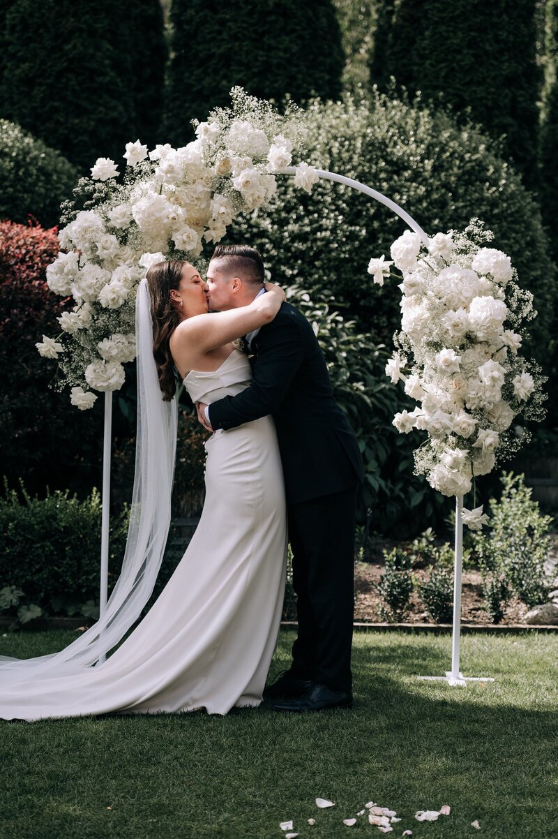 bride and groom first kiss under white floral archway in queenstown at their wedding