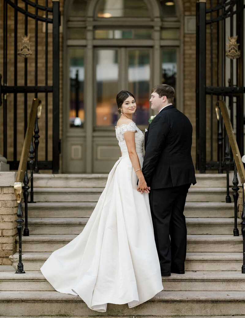 Bride standing gracefully as delicate details of her wedding gown are highlighted. A refined, intimate bridal moment captured in soft light