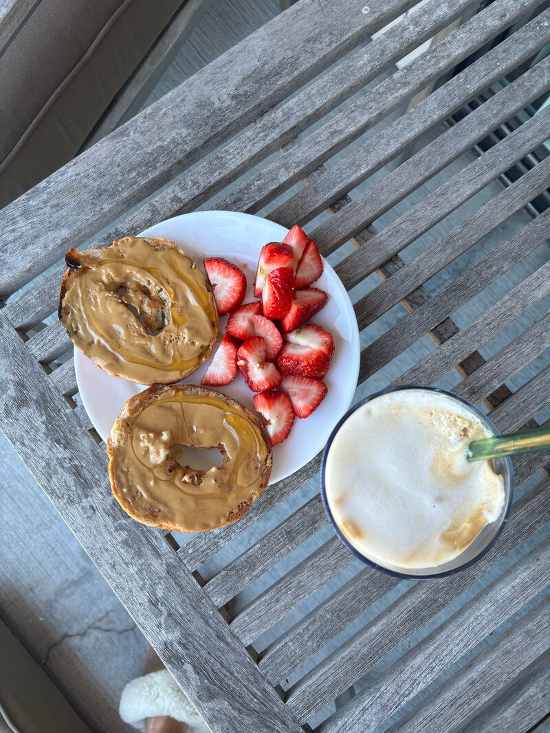 Image of a balanced breakfast: bagel topped with peanut butter and honey, cut strawberries, and a latte.