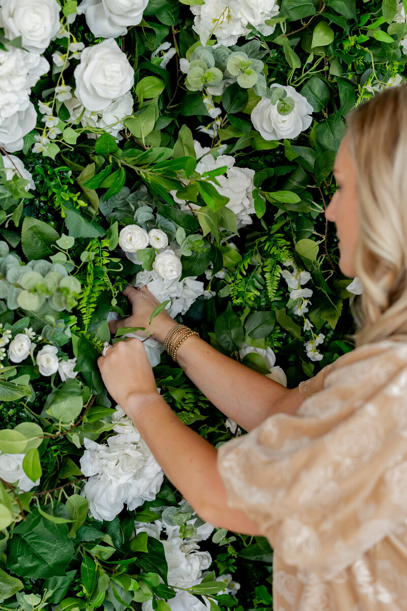Woman setting up green and white flower wall.