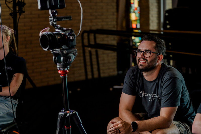Storyteller team member Chris leans forward in his chair as he performs an interview behind the camera.