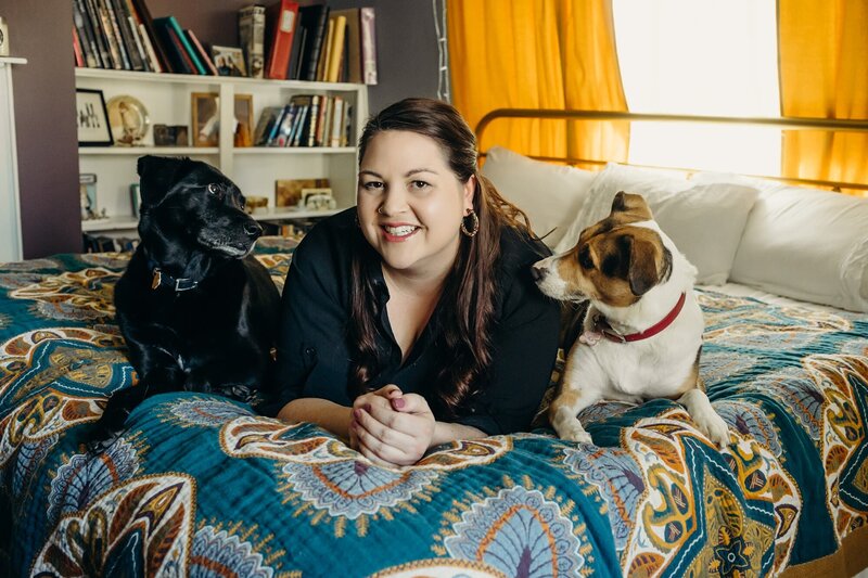 Alexa Nahas laying on her bed with her two dogs, smiling.
