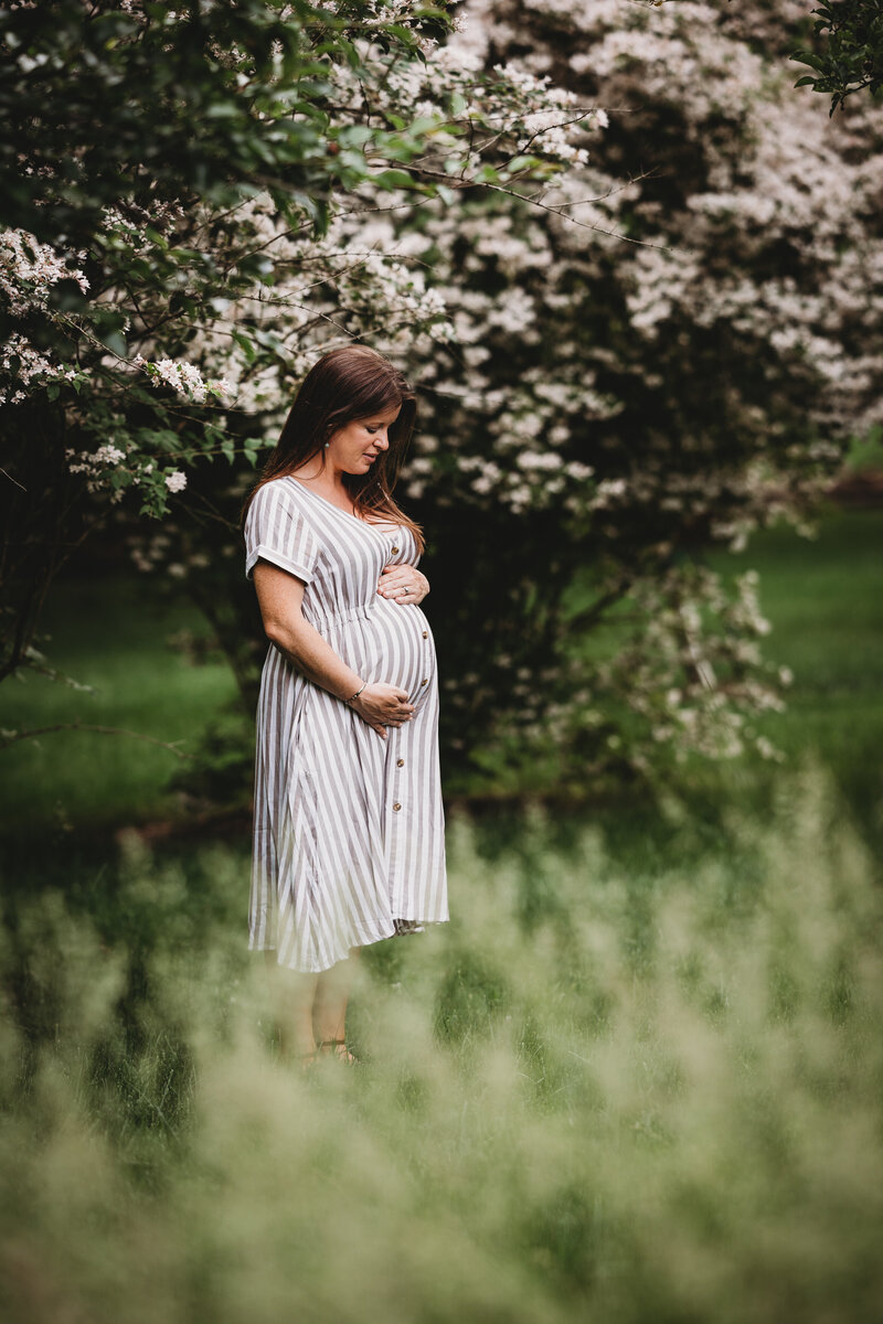 pregnant woman looking down and holding her belly in a striped dress