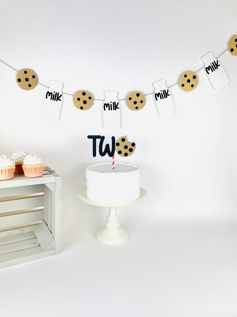 Two cake topper with milk and cookies, milk and cookies banner in back