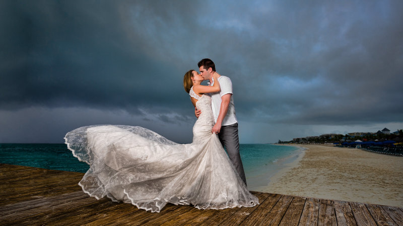 Bride and groom standing on a dock in Turks and Caicos with a stormy sky and ocean in the background, creating a striking wedding photo.