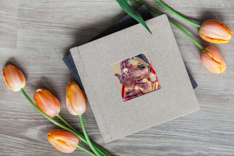 A flat lay picture of a wedding wedding album. A picture of a Indian women at her wedding. The wedding album is grey.