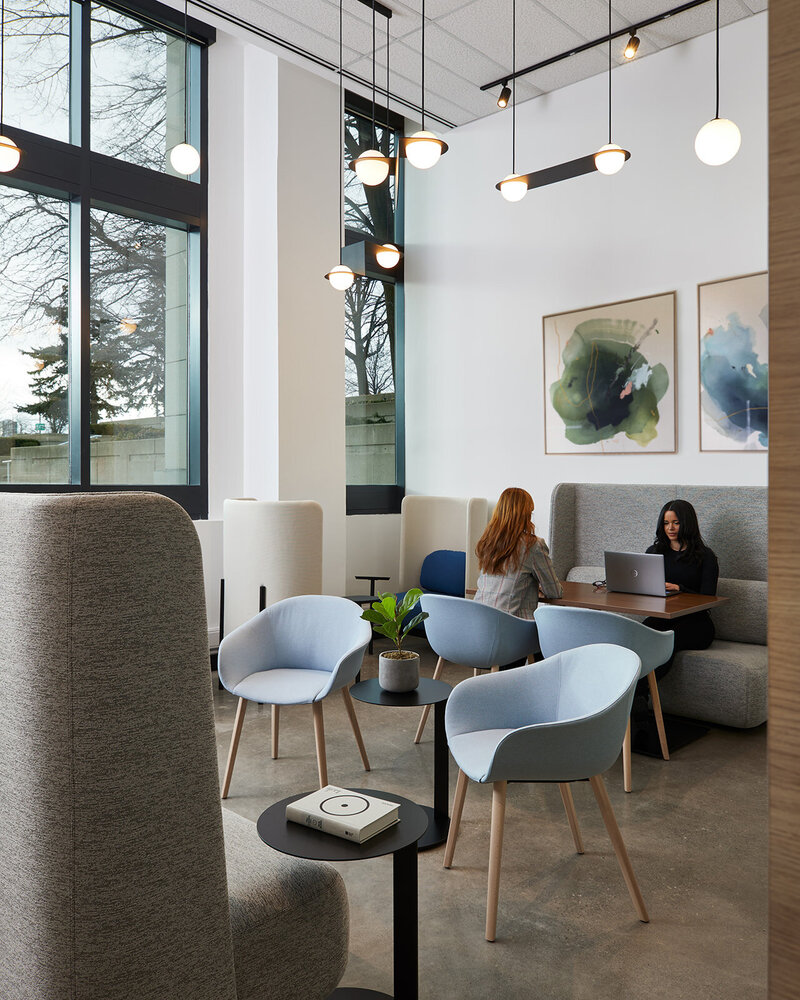 A bright, airy workspace with vibrant blue and green accents, globe lighting fixtures, and many chairs, benches, and tables