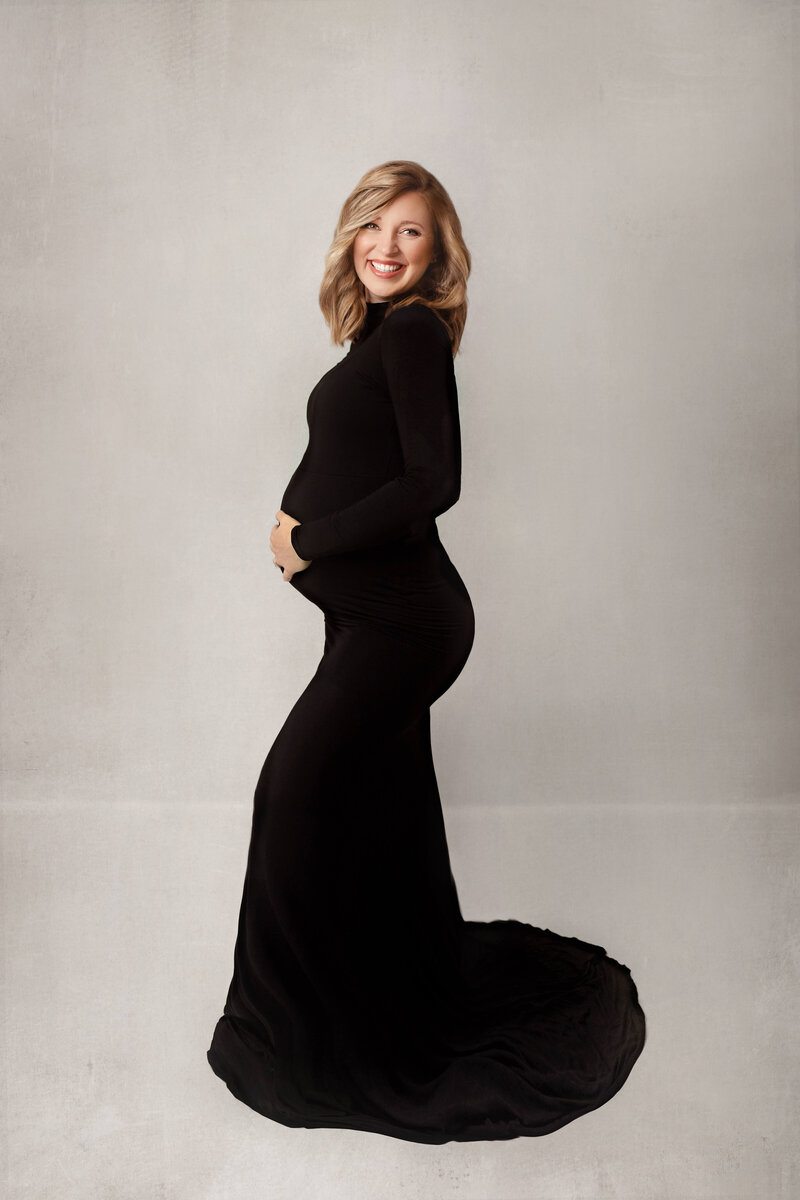 pregnant woman smiling holding her baby bump in black dress