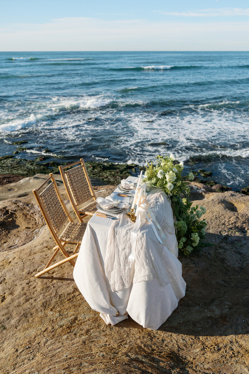 Elegant tablescape details with lush florals on the coastline, featuring an ocean backdrop, captured by a La Jolla wedding photographer.
