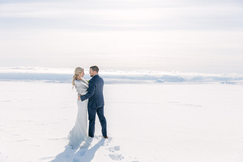 a bride and groom on top of a glacier in iceland looking at each other