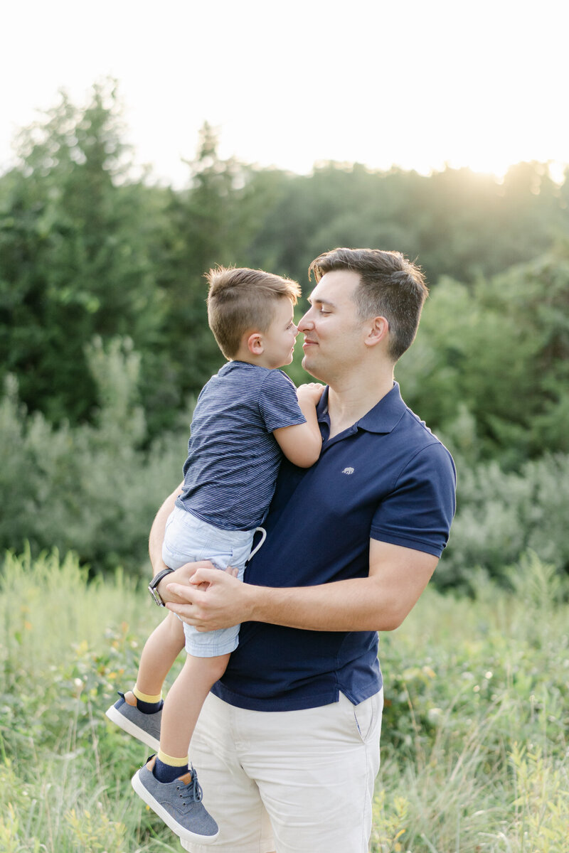 father in blue polo shirt kisses toddler son at sunset