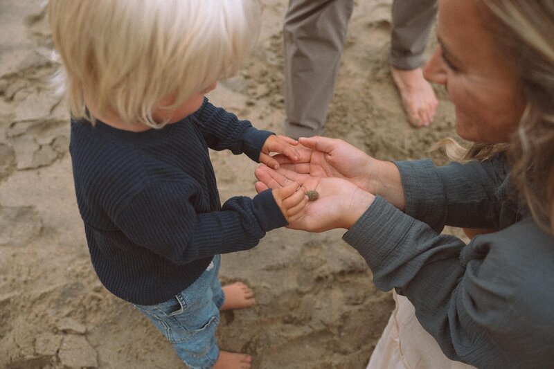 mother holding baby crab for son at beach