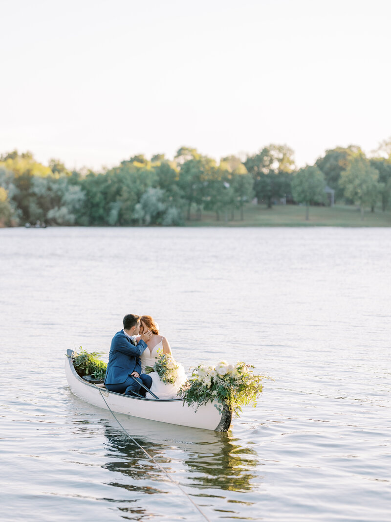 bride and groom kiss in a floral-filled canoe on a lake in Fayetteville, Arkansas