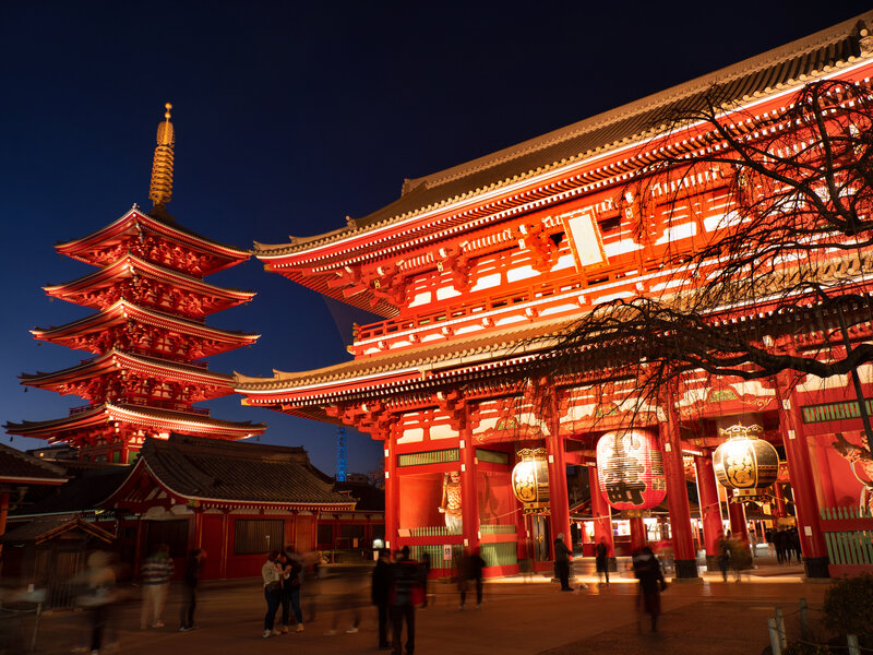 Evening view of Tokyo's iconic Sensoji Temple in Asakusa, beautifully lit with its vibrant red architecture glowing against a deep blue sky.