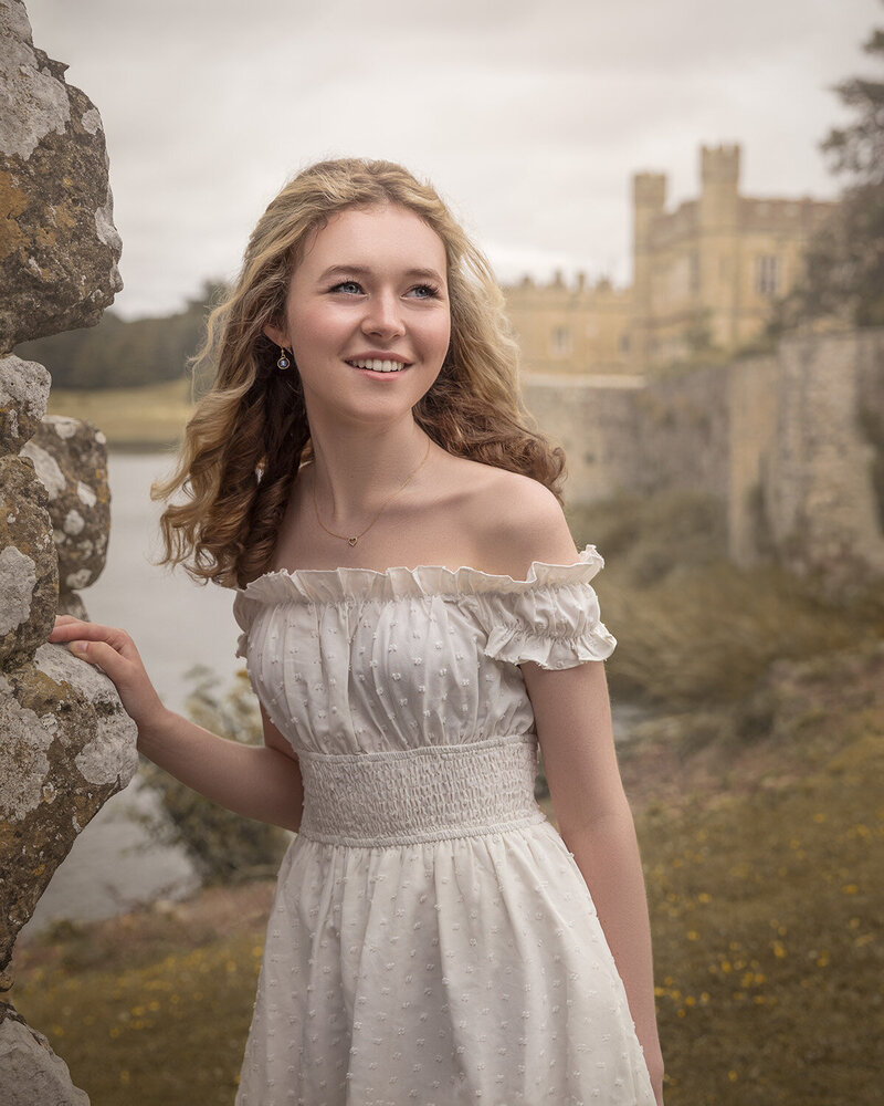 High school senior pictures taken at Leeds Castle, Kent. A young girl in a white dress posing by a wall with the castle in the background.