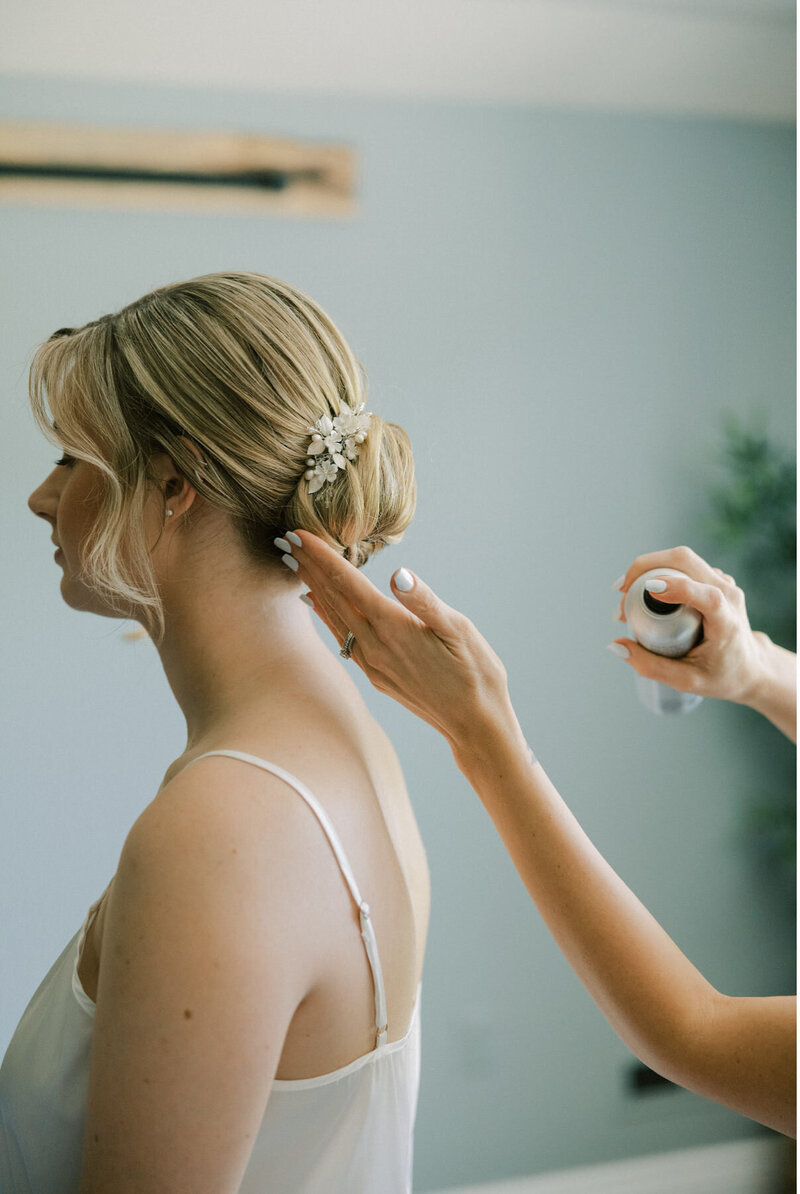 A side view of a bride's slick back bun getting final hairspray touches.