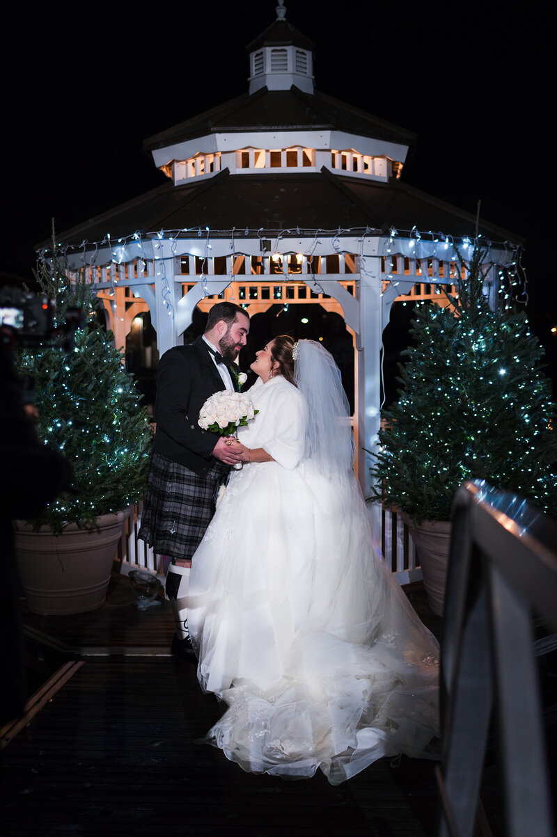 Night-time portrait of a Scottish dressed groom in a kilt with his Mexican bride in a princess gown in the gazebo at Russo's on the Bay in brooklyn.