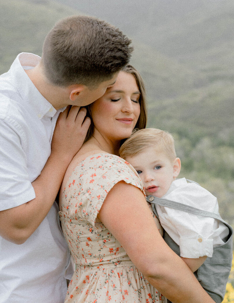 maternity session at the park with dad kissing mom and mom holding baby
