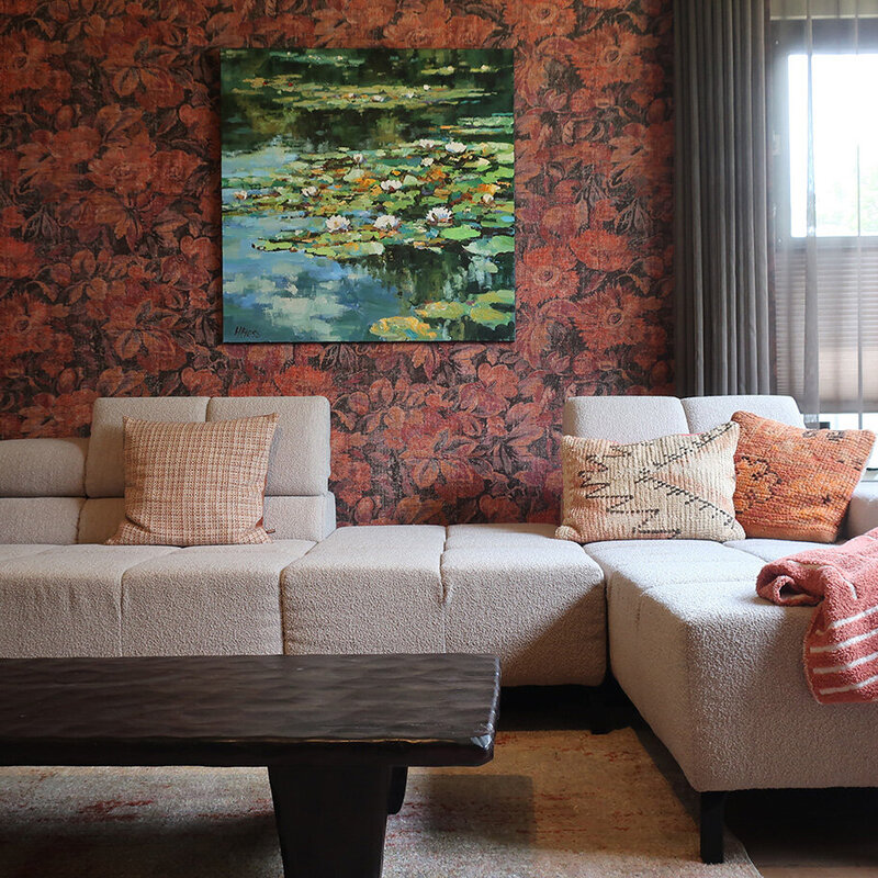 Zithoek met lichtbeige bank en oranje floral behang, afgewerkt met warme kussens en schilderij met waterlelies