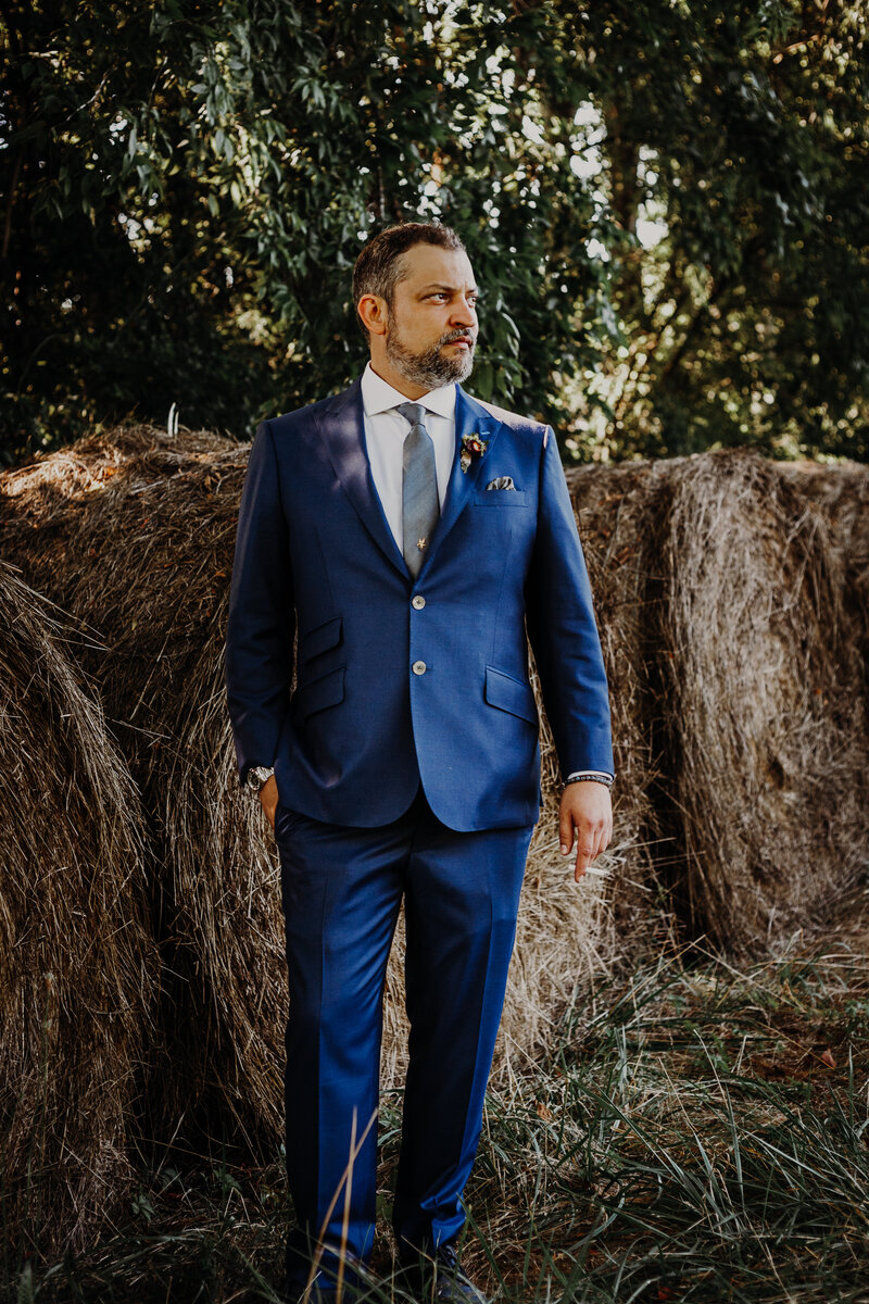 groom posing in front of a hay bale