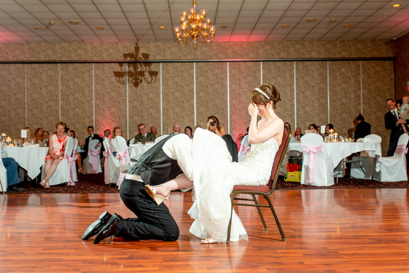 A groom ducks under the brides gown to retrieve the garter during their reception