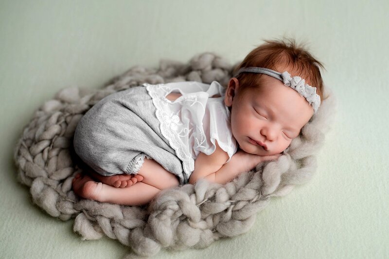 Newborn girl wearing a grey romper in bum-up pose on a sage blanket.