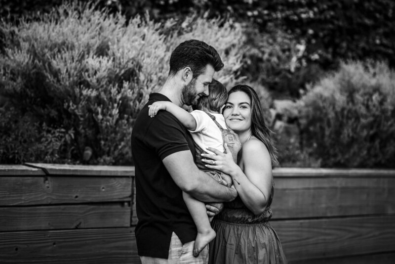mom looking at camera and hugging her son who is in her husband's arms as he smiles and looks down
