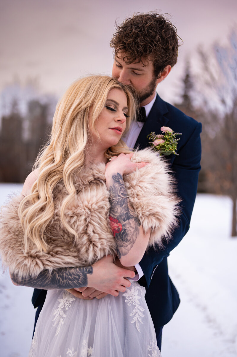 Groom kisses bride on temple during winter wonderland wedding at Kinsmen Park 
