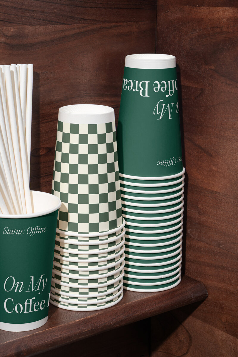 Branded green takeaway coffee cups with checkerboard pattern and typography for LUCCA Italian Sandwich Shop, highlighting packaging design.