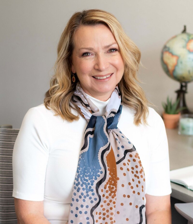 Francine in white blouse and orange and blue scarf sitting at grant writing desk smiling at the camera