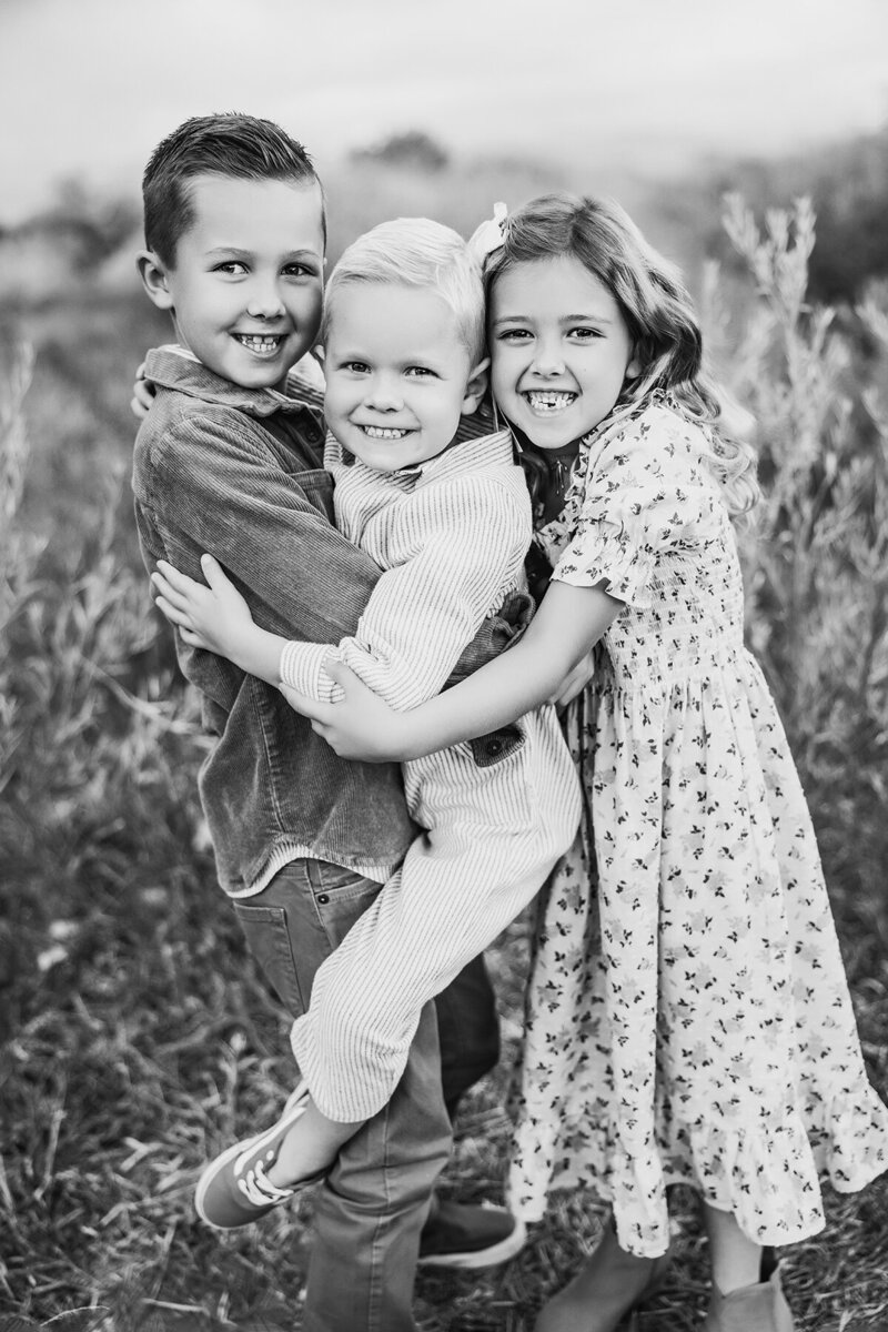 Black and white image of 3 siblings hugging each other