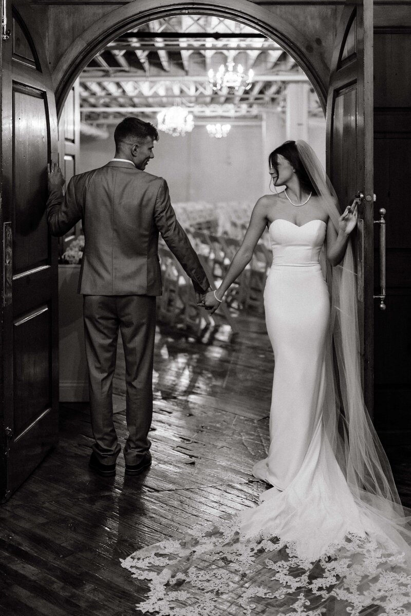 bride and groom stand in the doors of a chapel holding hands