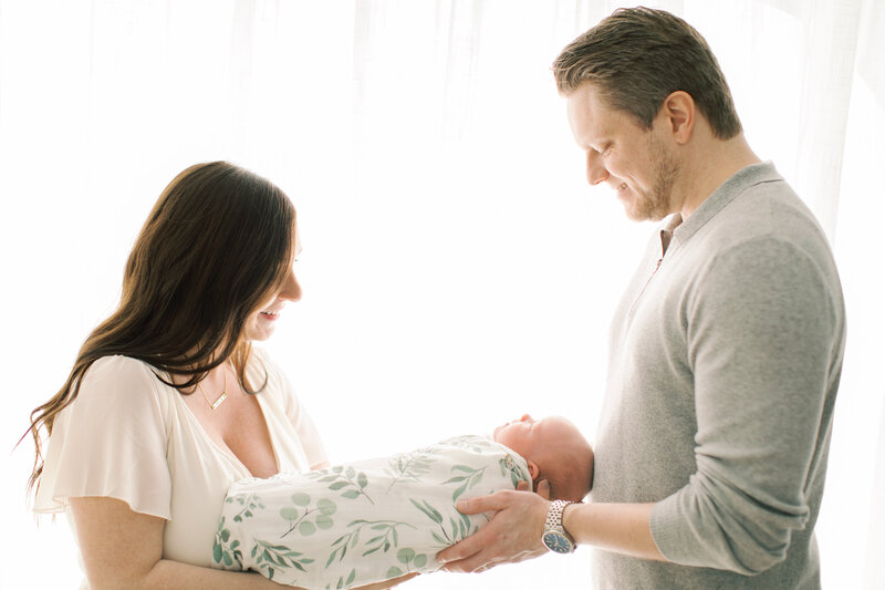 parents holding baby in front of window by Chicago Newborn Photographer