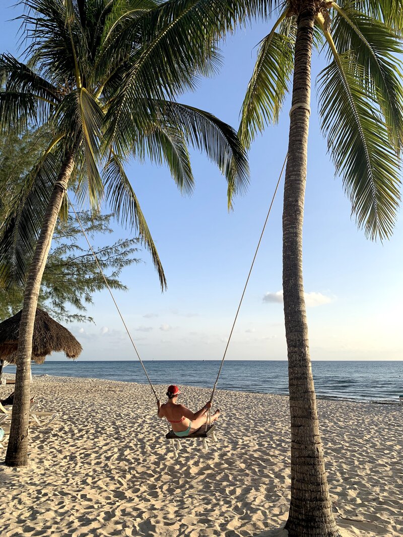 Woman swings between two palm trees at tranquil sandy beach