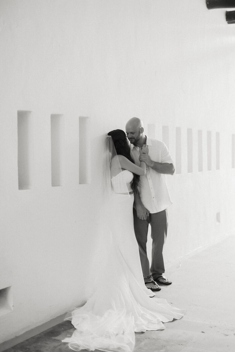 bride and groom embrace against white stucco wall