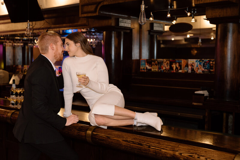 Elopement couple at a bar in Columbus. The bride is sitting on the counter with a drink while the groom is standing.
