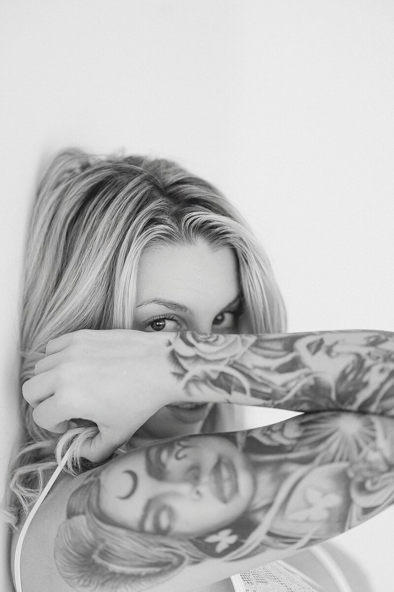 Black and white image of a woman with her tattooed arm covering most of her face below her eyes during her session with Indianapolis boudoir photographer, Brittney Lear.