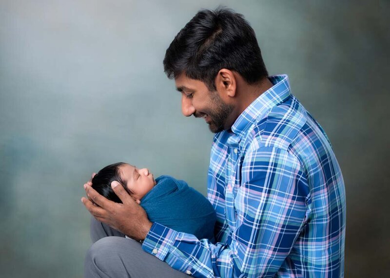 father-cradling-newborn-baby-blue-wrap