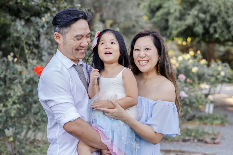 Young family sharing happy smiles during portrait session at Fremont Rose Garden in California