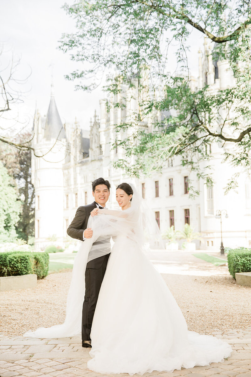 Bride and groom posing for a traditional fine-art wedding portrait in front of Château Challain, captured in a bright, elegant style.