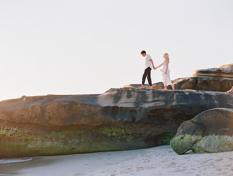 couple walking on beach rock with moss and beautiful sunshine