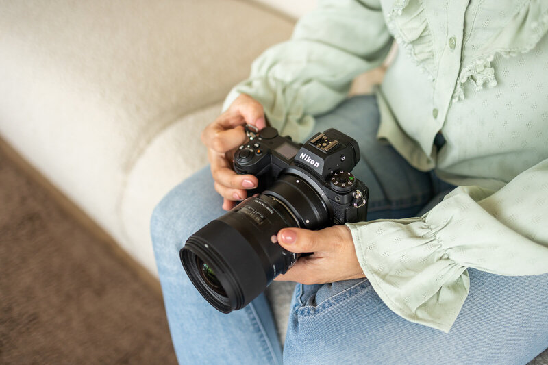 Vrouw houd haar camera in de hand vast, zittend op een bank