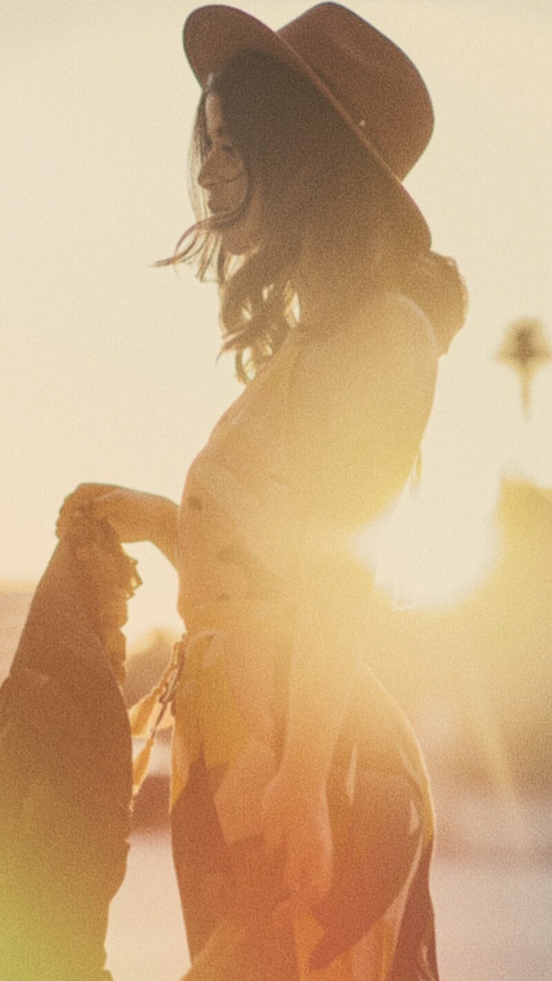 image of young woman sideways wearing a hat with sun backlit