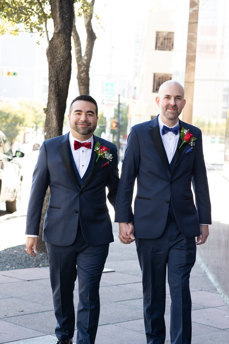 Two grooms in tuxedos walking down the street captured by an Austin wedding photographer.