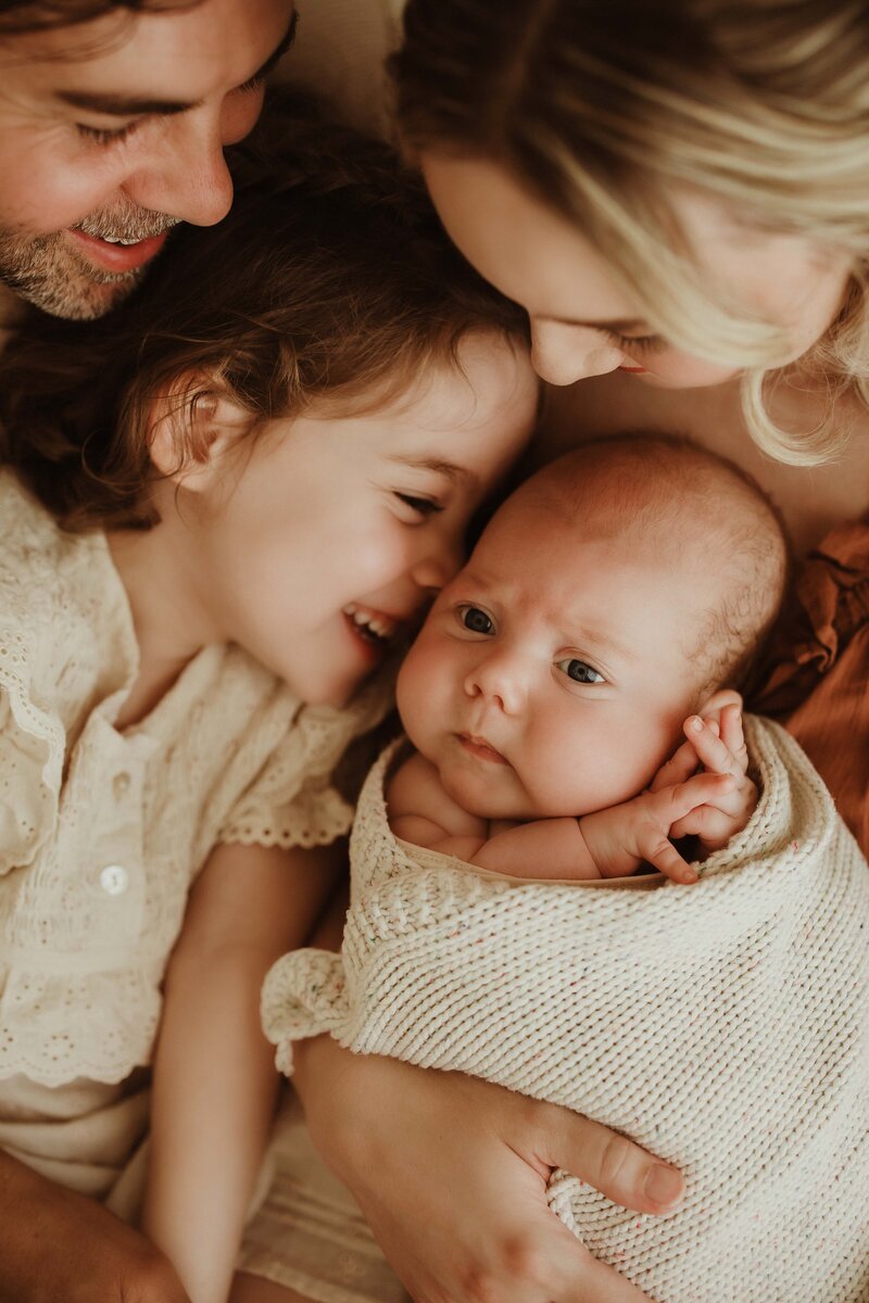 Parents cuddling newborn baby with sibling smiling, captured by Sydney newborn photographer Sophie Lea.