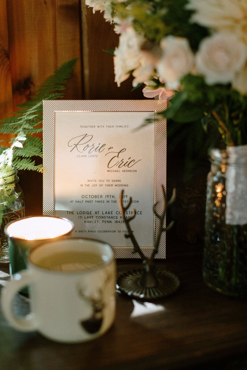 A wedding invitation framed, surrounded by candles, flowers, and rustic decor, inviting guests to celebrate a marriage union