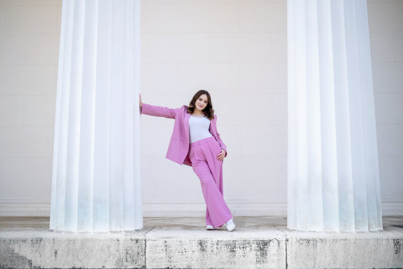 Founder leaning against a white column, wearing a full pink suit, smiling