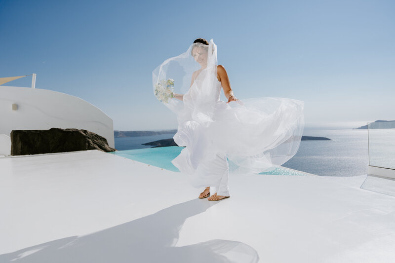 Santorini wedding, bride getting her dress blown in the wind at Dana Villas